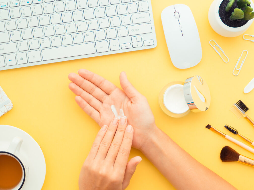 Cosmetic Solutions Account Management Image features a models hands near a computer mouse and keyboard. The model is applying private label skincare cream into her hands.