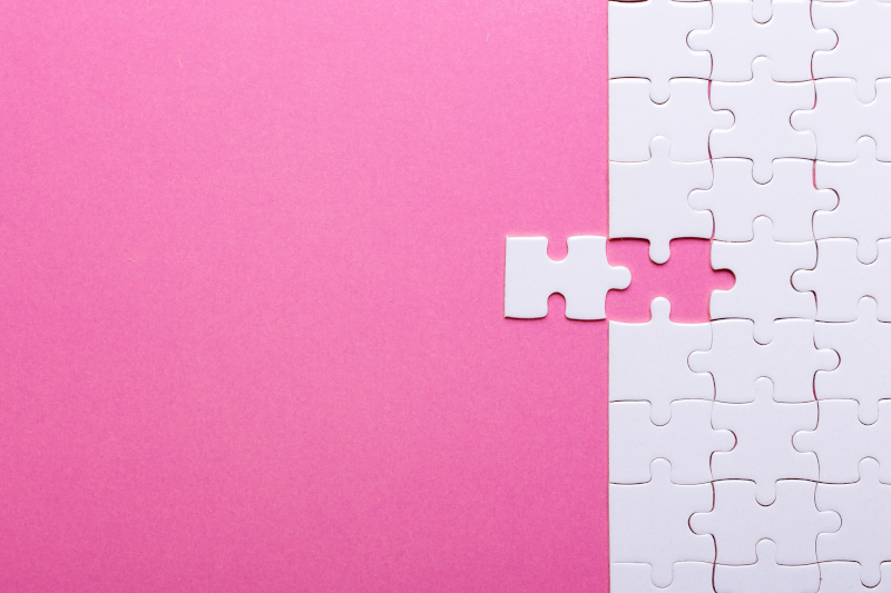 Private Label Skincare manufacturers Cosmetic Solutions White Space Mapping Image features a White puzzle piece being slotted into a blank white puzzle. The puzzle sits on a pink background