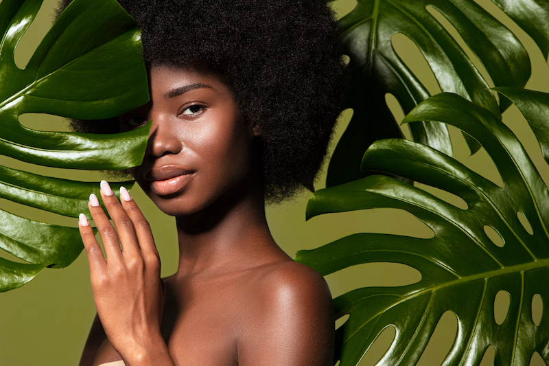Connected with a nature. Beauty portrait of young beautiful african american woman with posing against green exotixc plants background. Natural skin care concept
